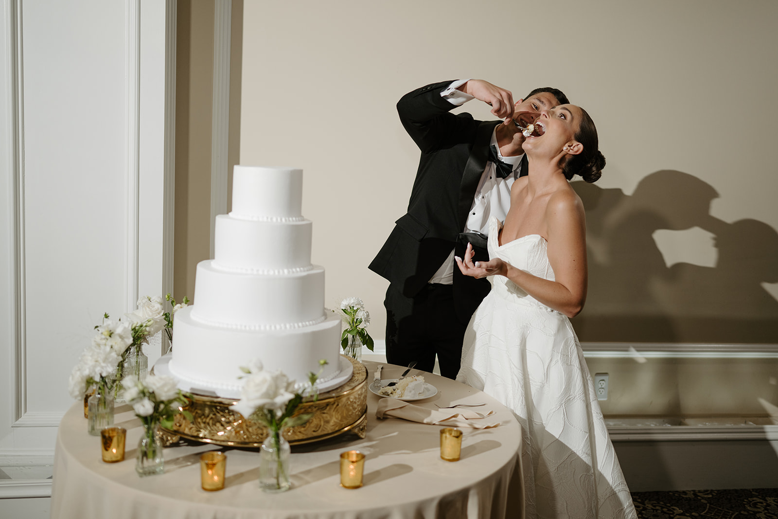 Groom feeding a bite of wedding cake to the smiling bride during their reception cake cutting.